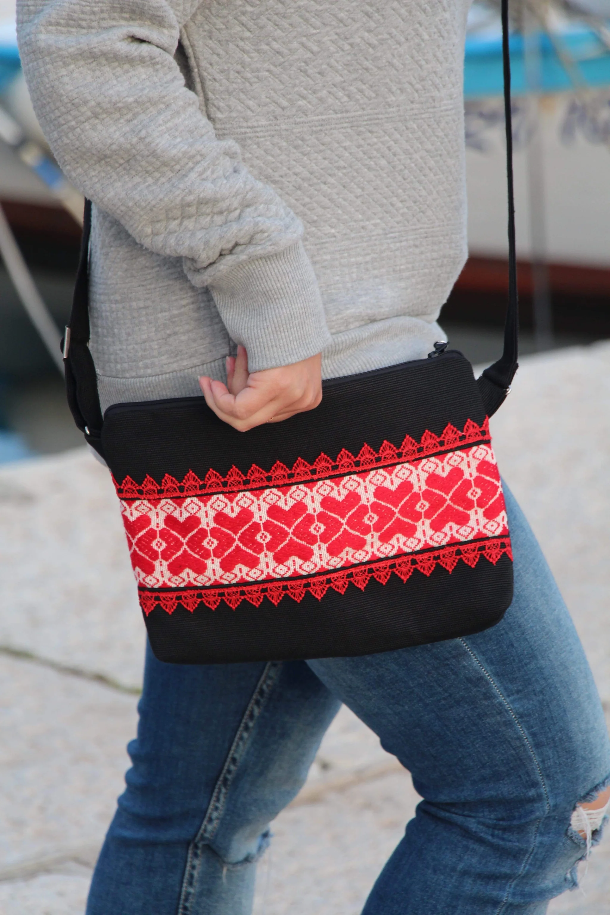 Close-up of a person holding a black crossbody bag with red and white heart-patterned trim, wearing jeans